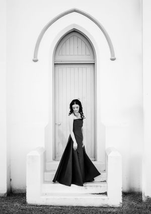 A dramatic navy dress captured in black and white against architectural arches and a pale door.