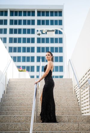 Elegant black dress pose on modern concrete staircase with glass building background.