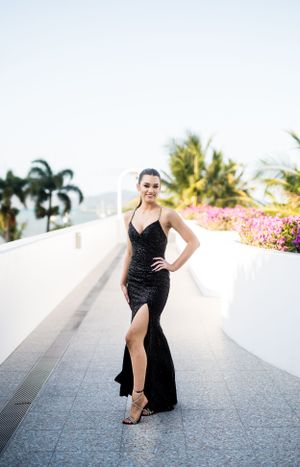 Elegant formal portrait in a black evening gown on a tropical pathway with palm trees.