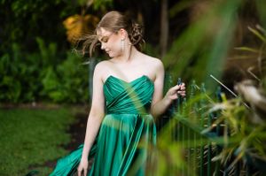 A woman in an emerald green evening gown poses gracefully in a lush garden setting.