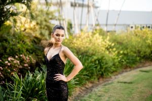 Formal portrait in a sparkling black gown amid tropical garden setting.