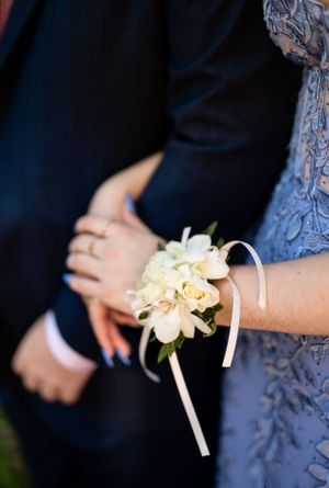 Close-up of delicate white rose corsage with ribbon worn on formal attire.