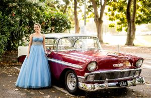 A light blue ballgown paired with a classic burgundy 1956 Chevrolet Bel Air in an outdoor setting.