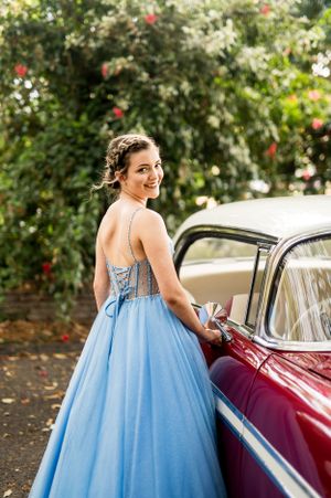 A stunning blue formal gown with detailed bodice photographed beside a classic burgundy car.