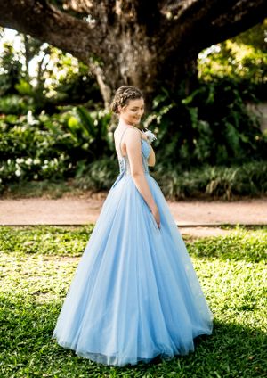 An elegant blue tulle ball gown photographed in a serene garden setting under large trees.