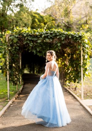 A whimsical light blue formal dress photographed in motion along a garden walkway with overhead vines.