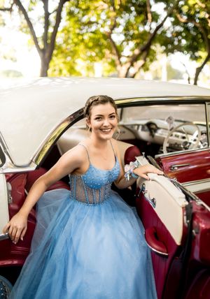 A blue ballgown with sparkly bodice worn while seated in a classic burgundy and cream car.
