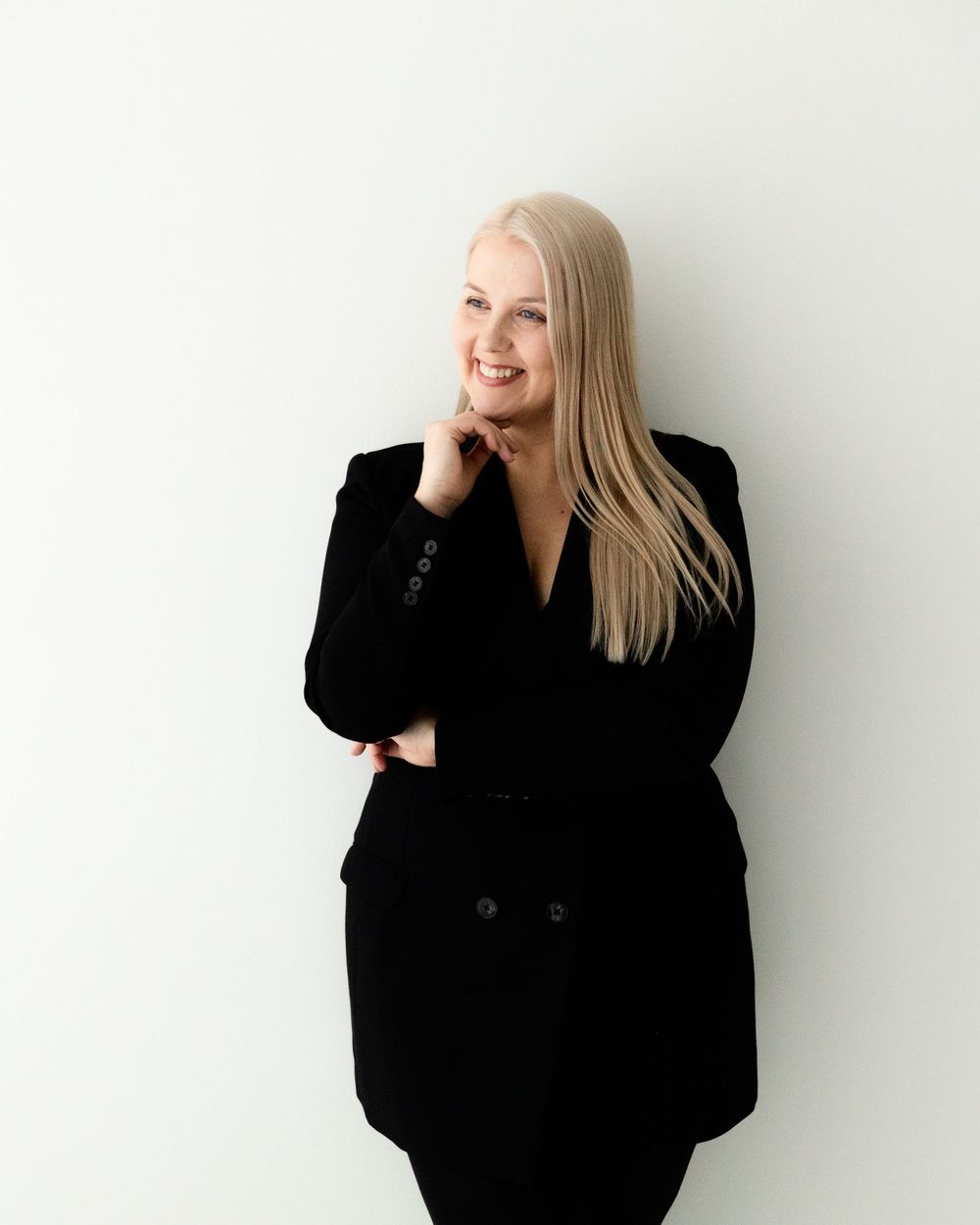 Professional portrait showing a person in a black blazer smiling while posing against a white background.