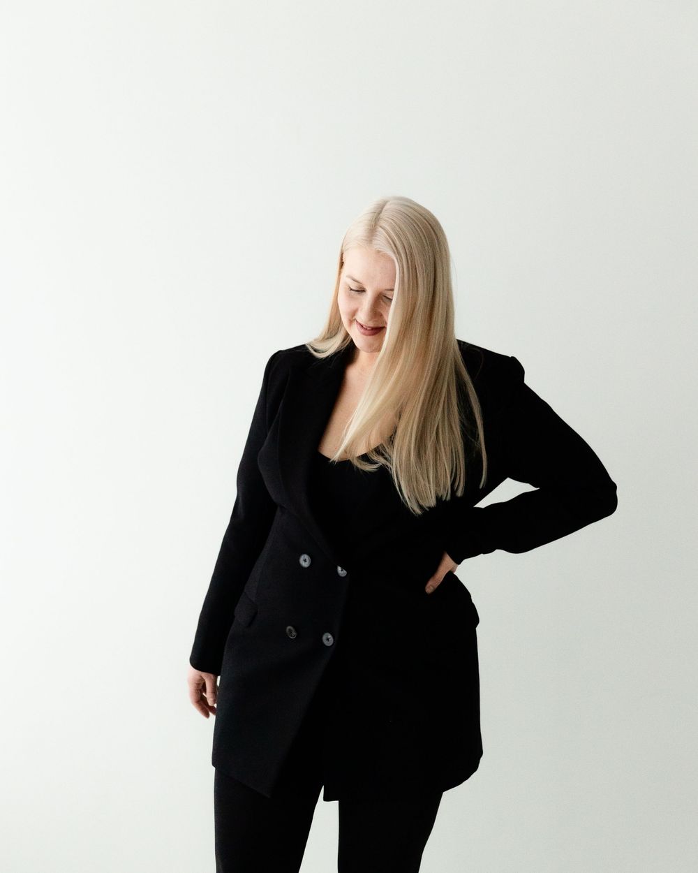 Person in a stylish black blazer and pants poses against a white background with one hand on their hip.