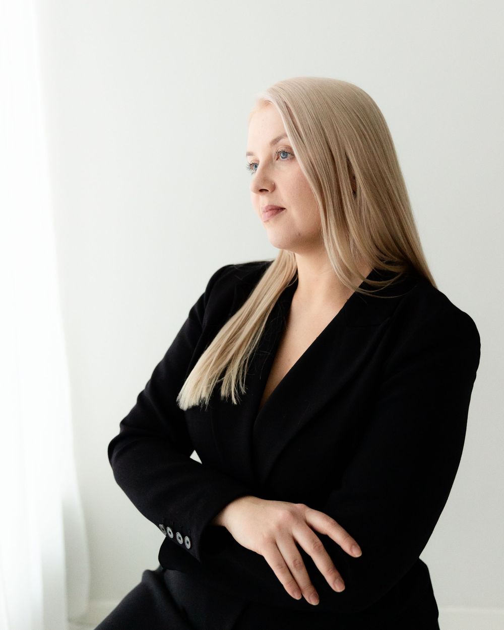 Professional portrait of a person in a black blazer against a white background looking to the side.