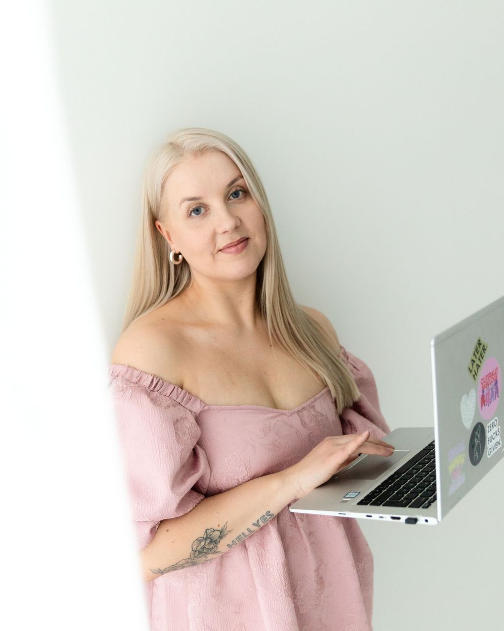 Woman in pink off-shoulder dress working on laptop with stickers against white background.