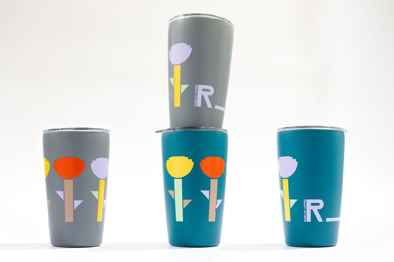 Colorful reusable coffee tumblers with flower designs stacked together in gray and teal colors.