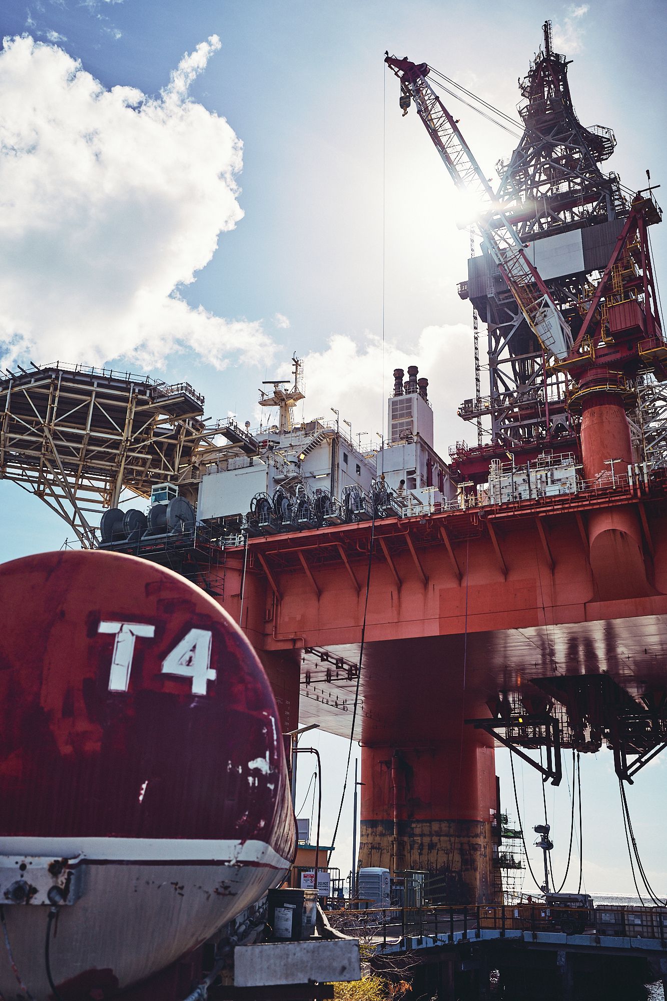 Large red offshore drilling platform with T4 marking against bright blue sky.