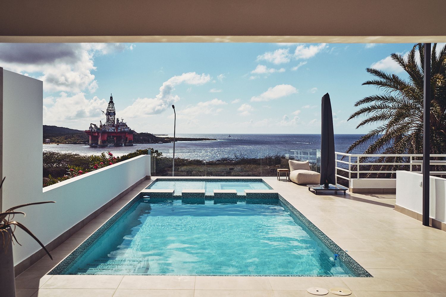 Modern infinity pool overlooking the ocean with palm trees and lighthouse in the distance.
