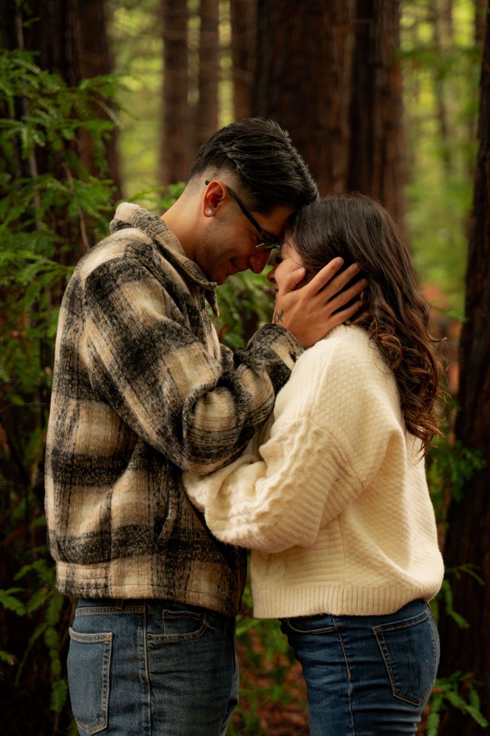 Romantic couple sharing intimate moment in forest wearing coordinated sweater and plaid outfits.