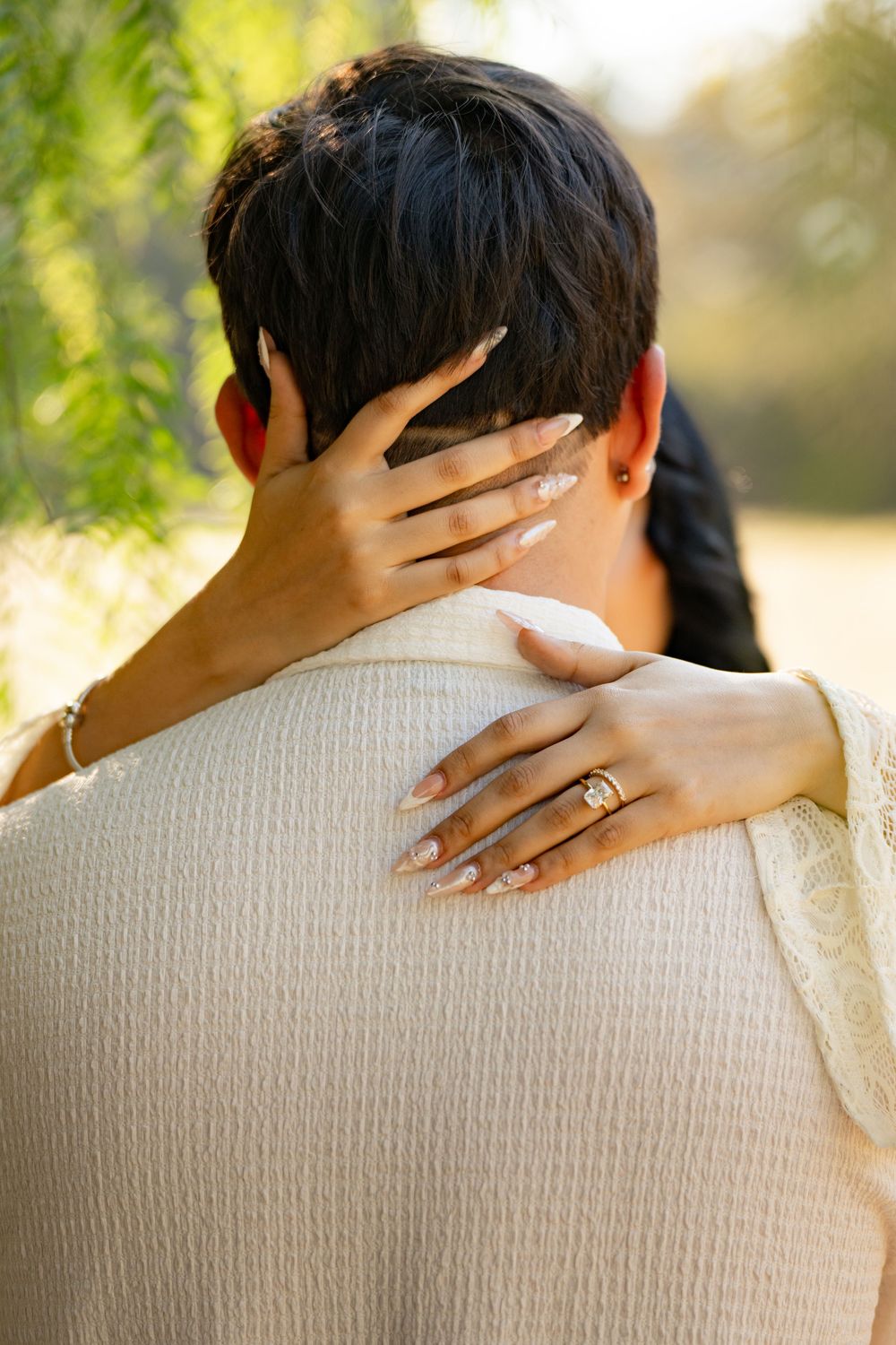 Close-up of hands embracing with an engagement ring visible against a cream colored sweater in natural lighting.
