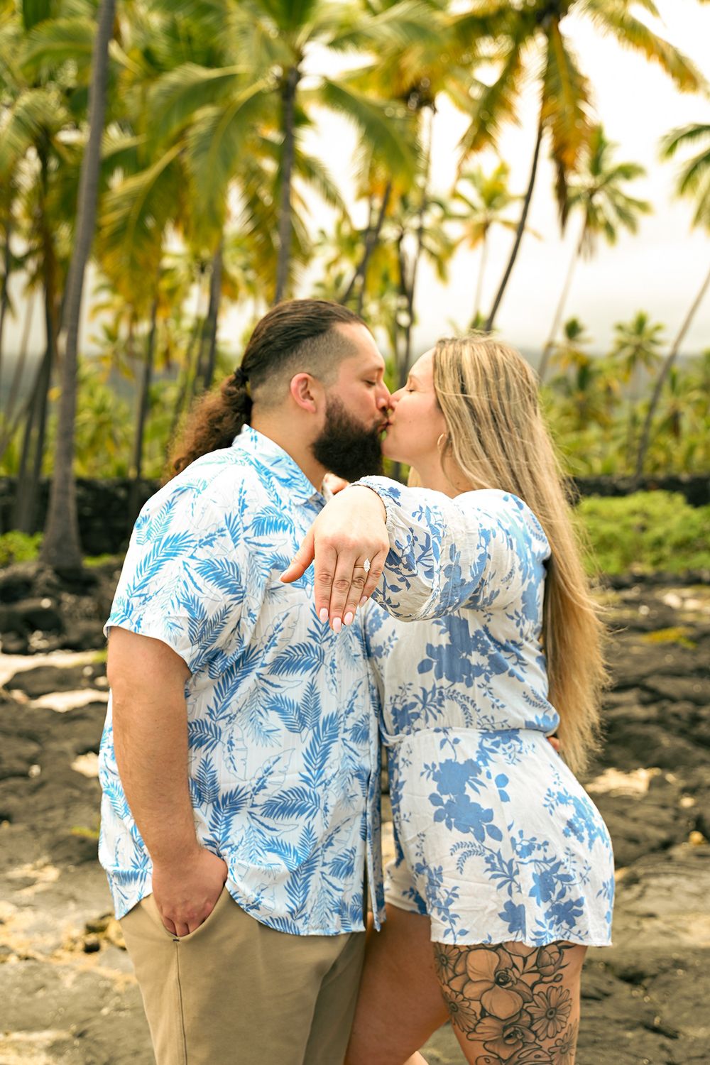 A couple in coordinating blue and white outfits embraces on a Hawaiian beach.