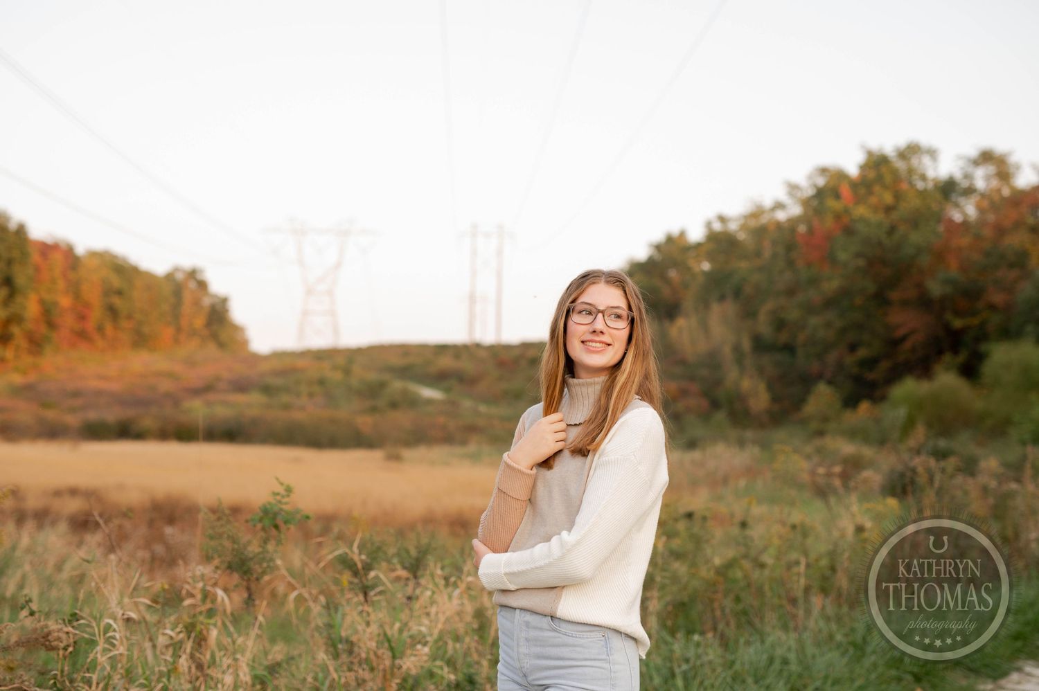 Outdoor portrait in beige sweater against autumn field and sunset sky.