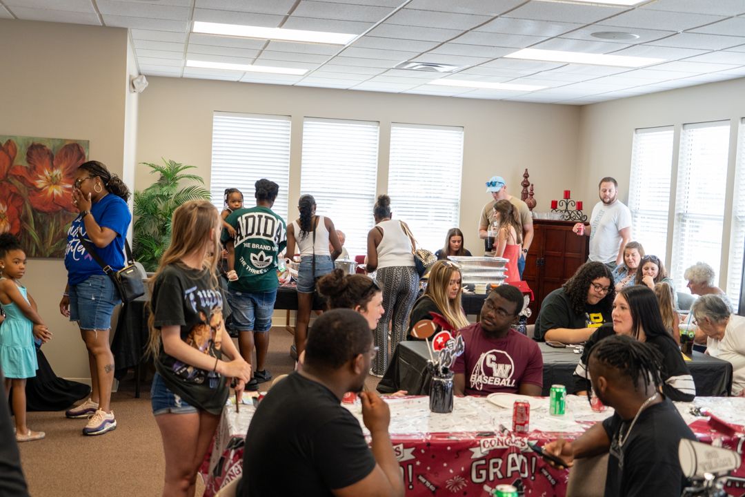 Students gather in a classroom for a casual social event with refreshments and decorations on tables.