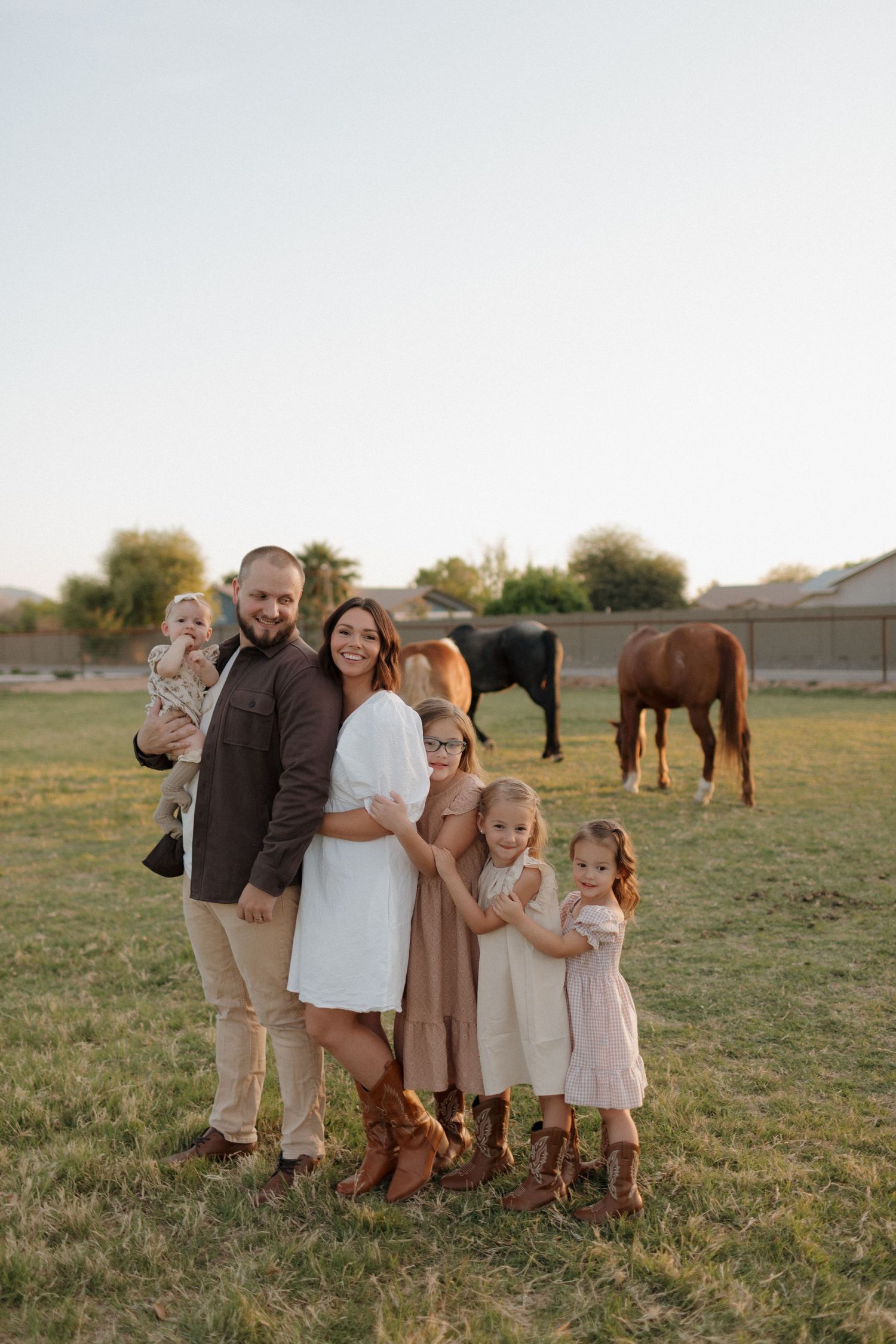 A family portrait in a field with horses grazing in the background during golden hour.