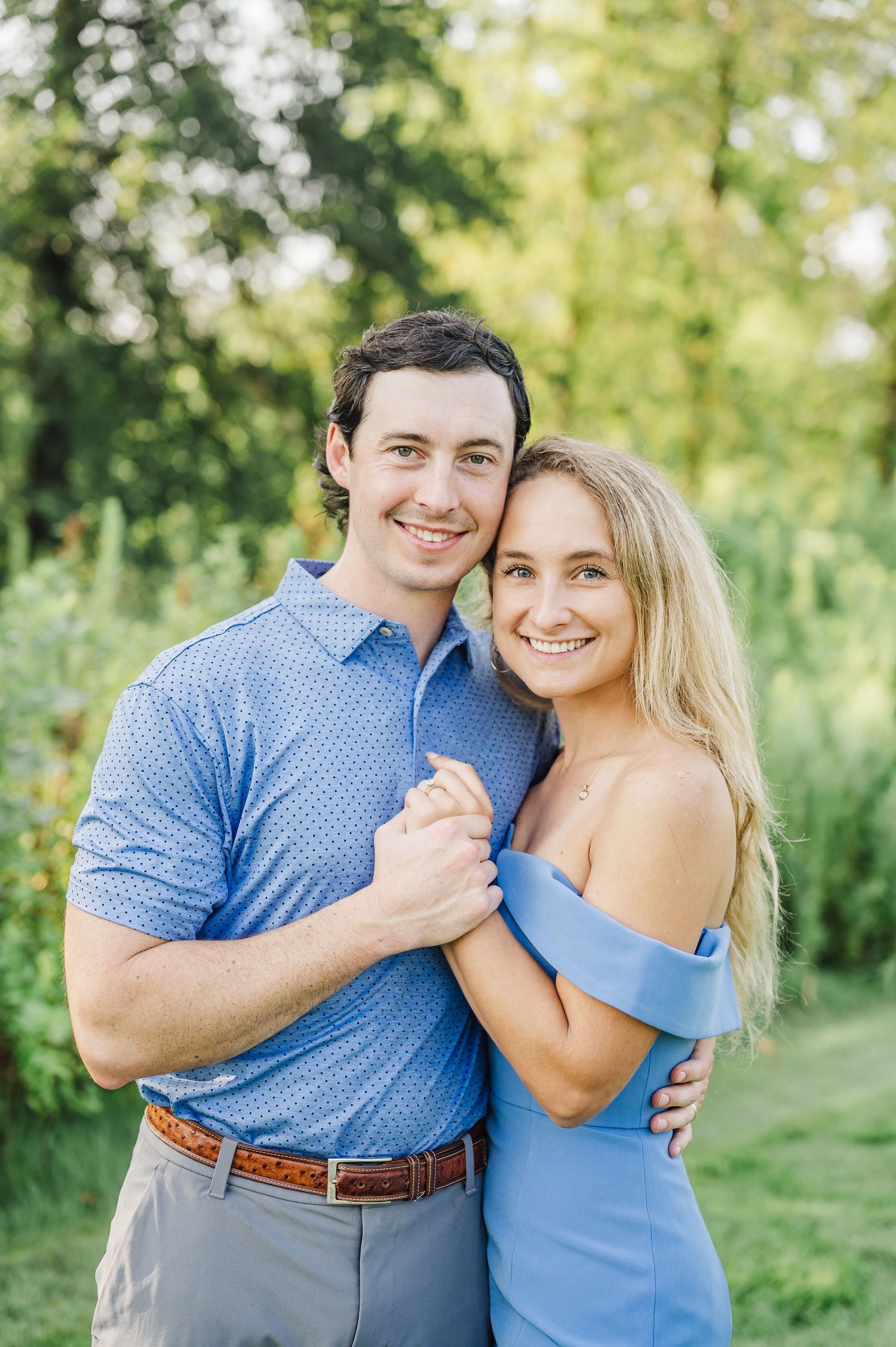 Sweet couple embracing outdoors in blue coordinated outfits against lush green background.