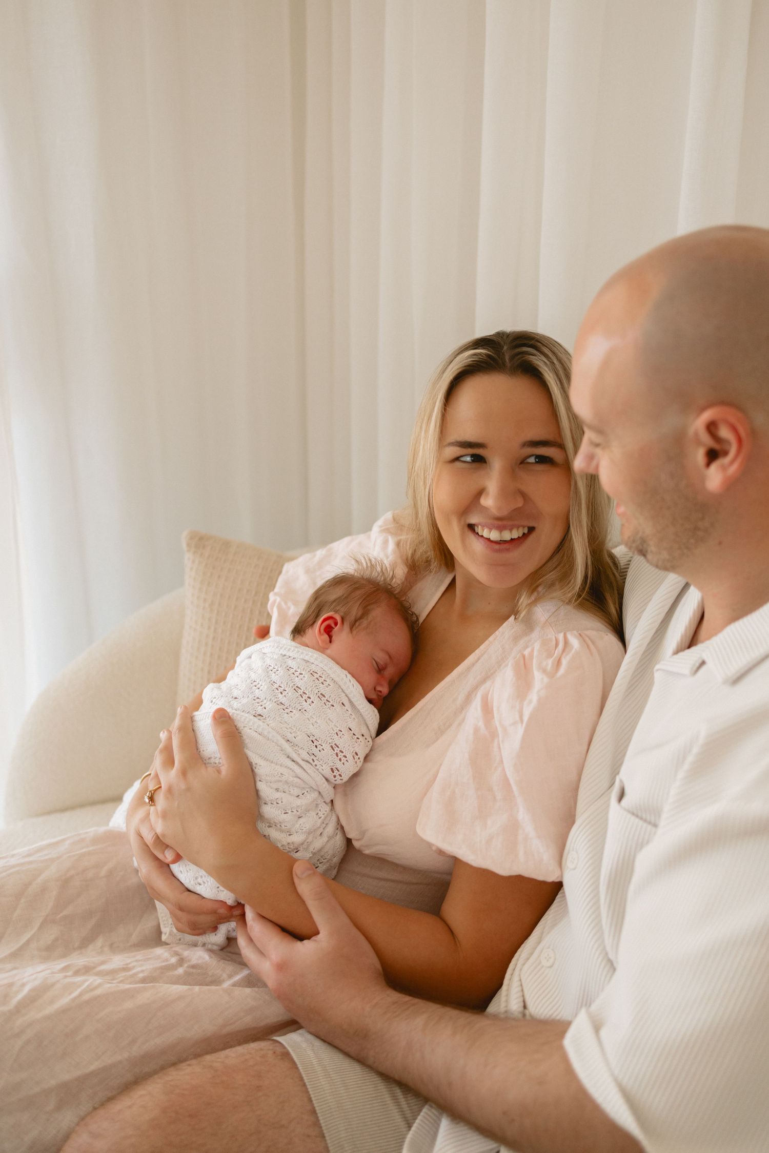 A series of tender moments between parents and newborn baby in a bright, white bedroom setting.