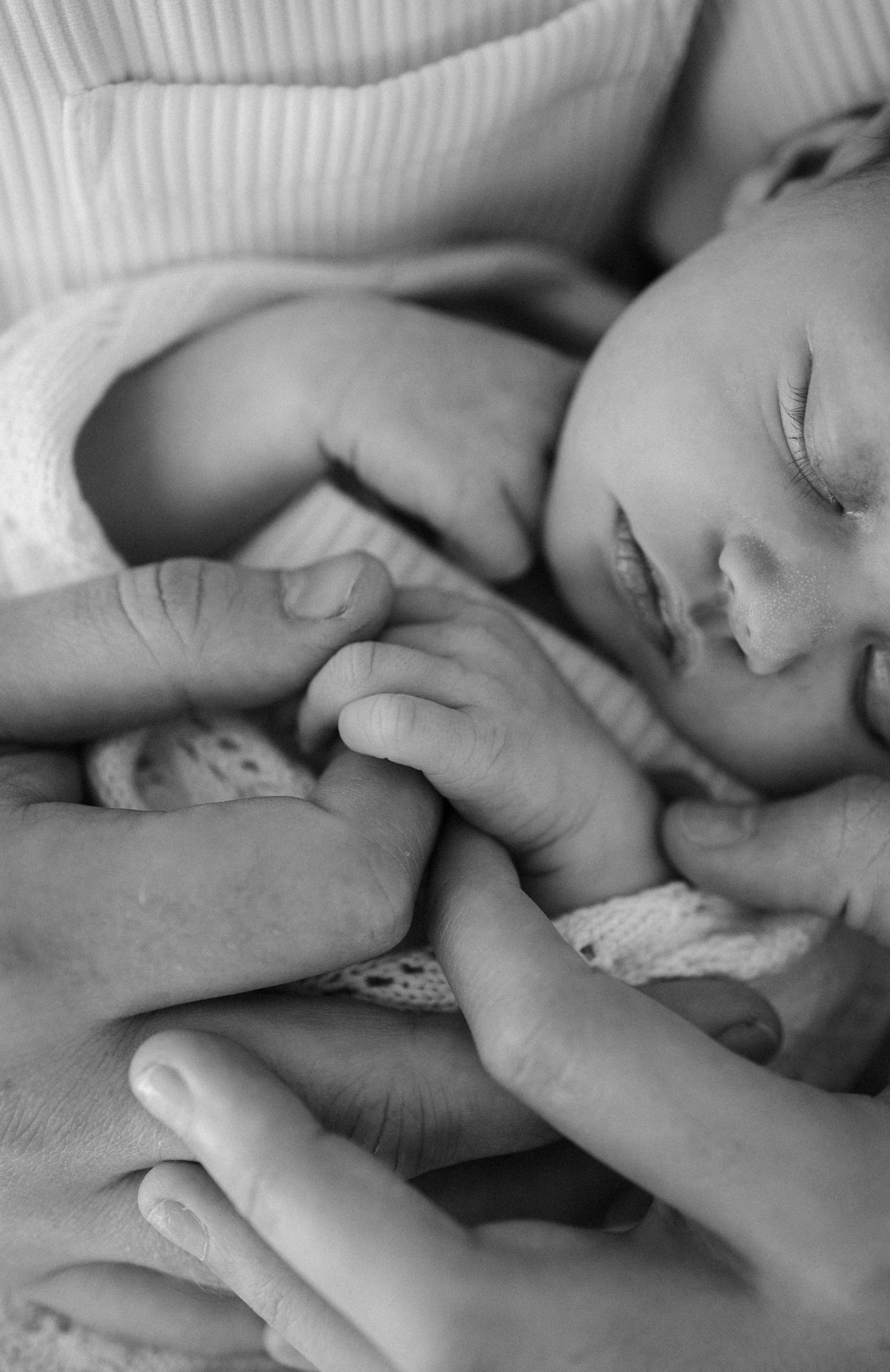 Black and white close-up image of newborn baby hands grasping fingers together in a tender moment.