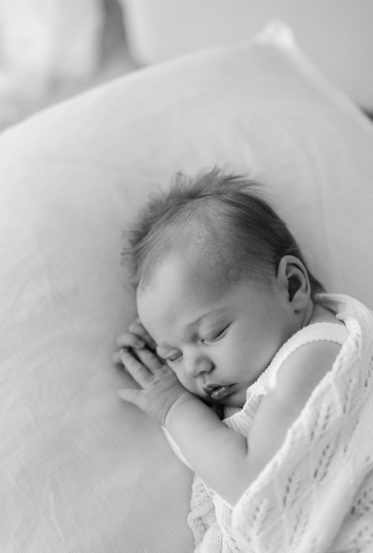 A peaceful black and white image of a sleeping baby wearing white lace swaddle against soft bedding.