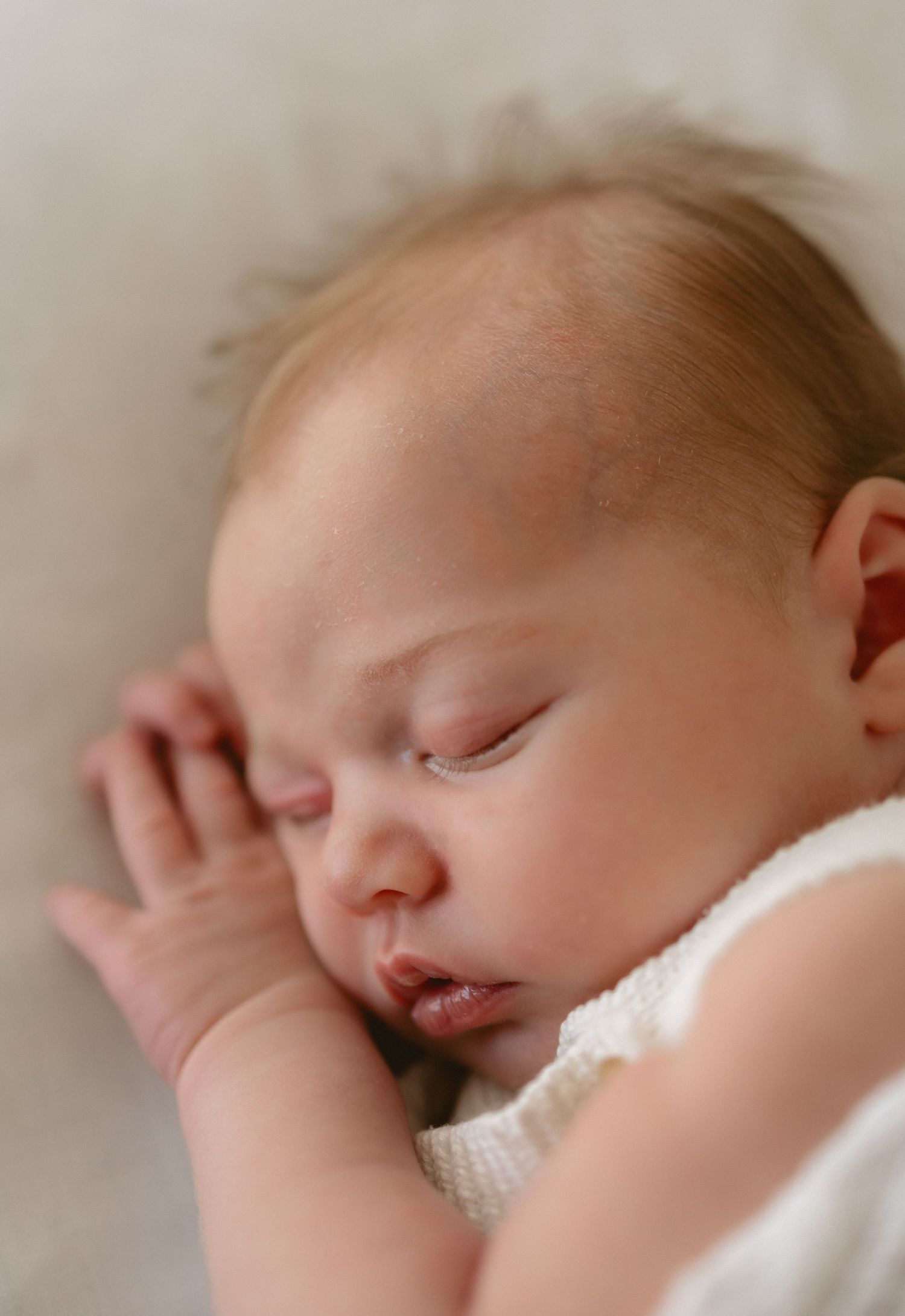 A peaceful sleeping newborn wearing a white outfit is captured in a gentle close-up photoshoot sequence.