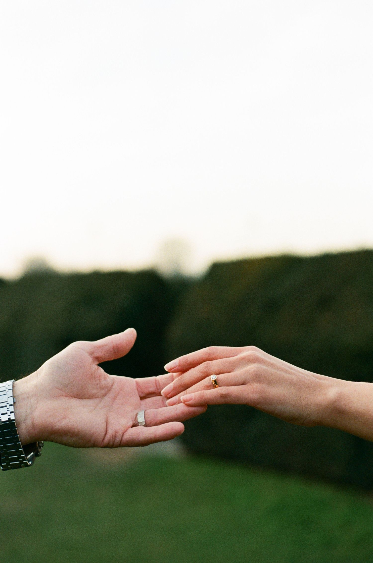 Two hands reach towards each other with one wearing a watch and the other displaying an engagement ring in a romantic moment.