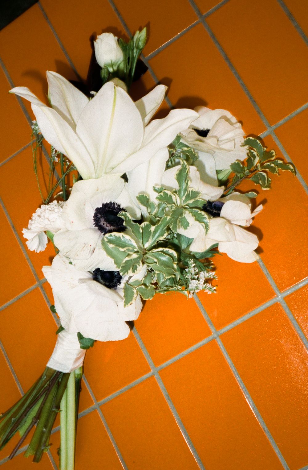 A beautiful white bridal bouquet with lilies and anemones against orange terracotta tiles.