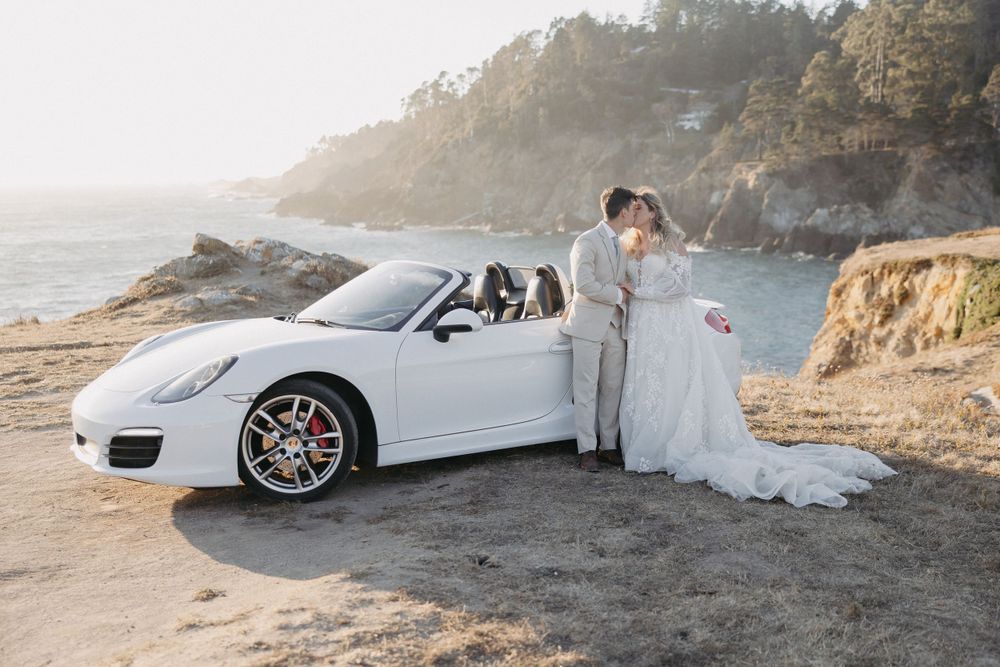 An elegant white Porsche convertible parked on a scenic coastal cliff during a sunset wedding photoshoot.