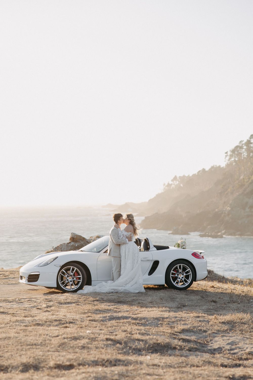 A seaside wedding portrait with a white Porsche convertible against a coastal cliff backdrop.