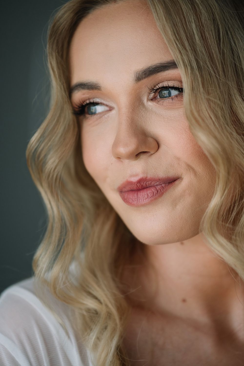 Close up beauty portrait of a woman with wavy blonde hair and natural makeup against dark background.