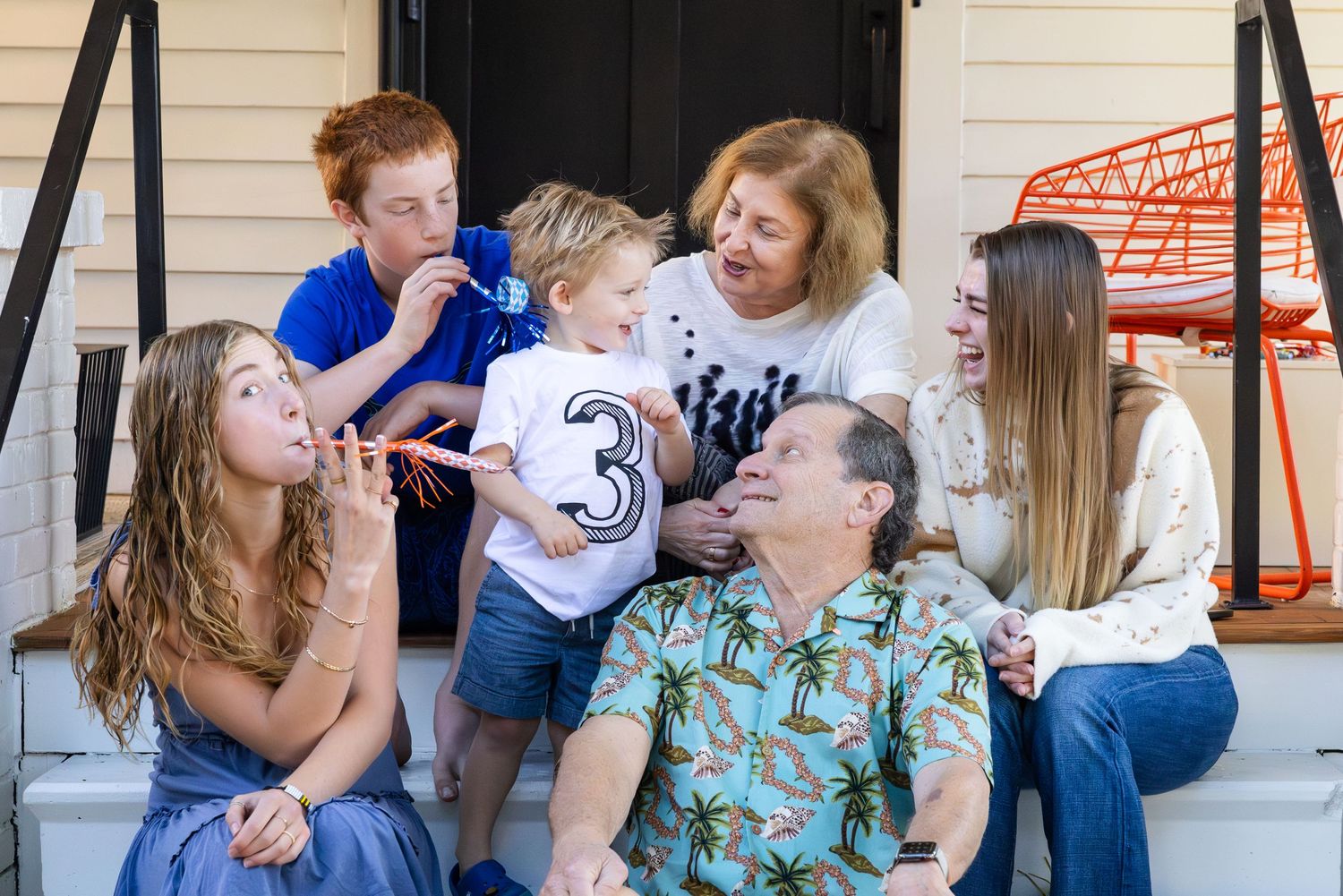 A cheerful group shares laughter while sitting together on outdoor steps during a candid family moment.