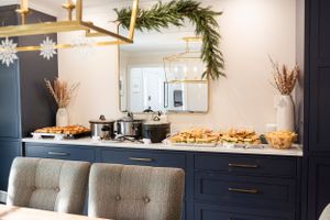 A buffet setup with chafing dishes on a white countertop against navy cabinets with holiday greenery and gold accents.