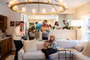 A modern living room with a circular chandelier where people relax and socialize on a beige couch.