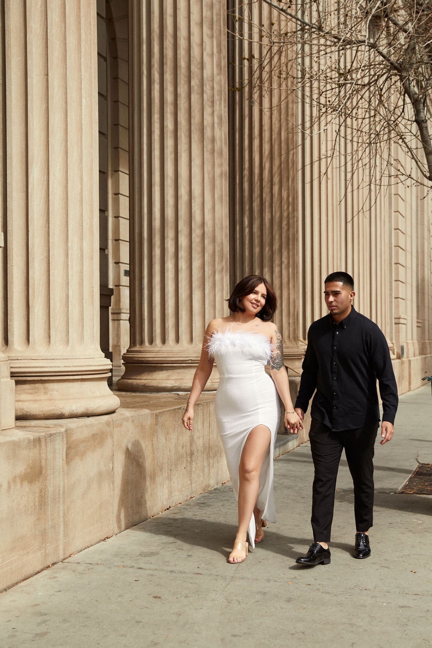 Couple walks hand in hand along colonnade with classical architecture.