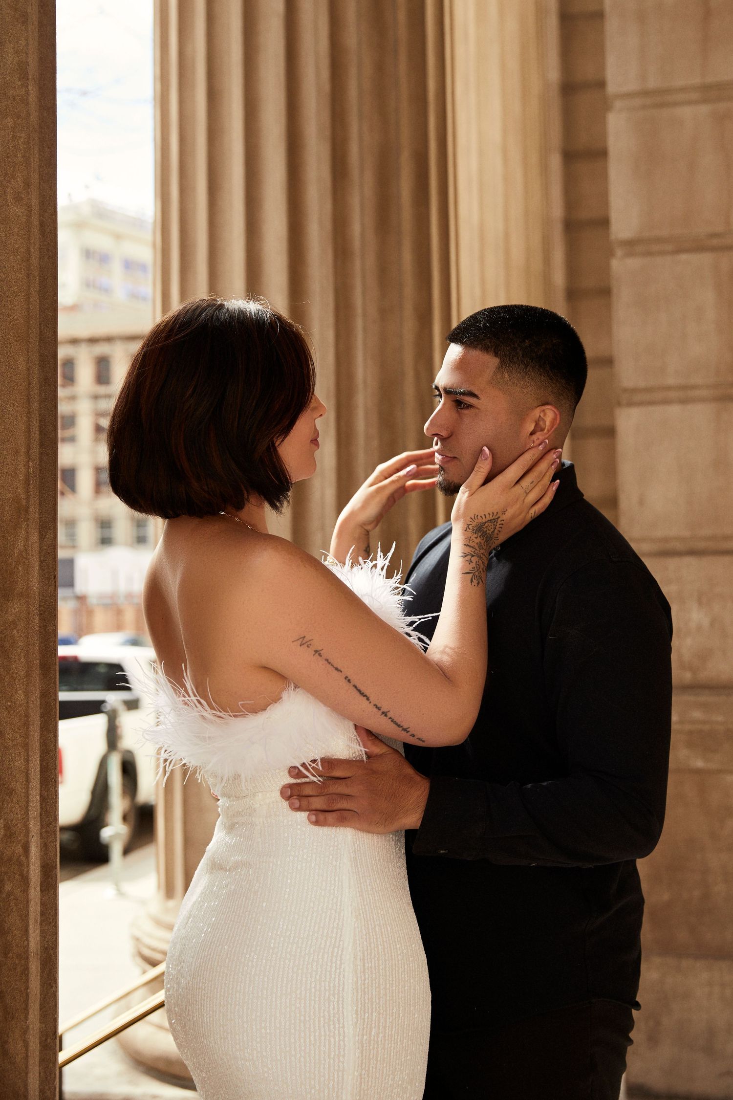 Couple embraces between classical stone columns in warm sunlight.