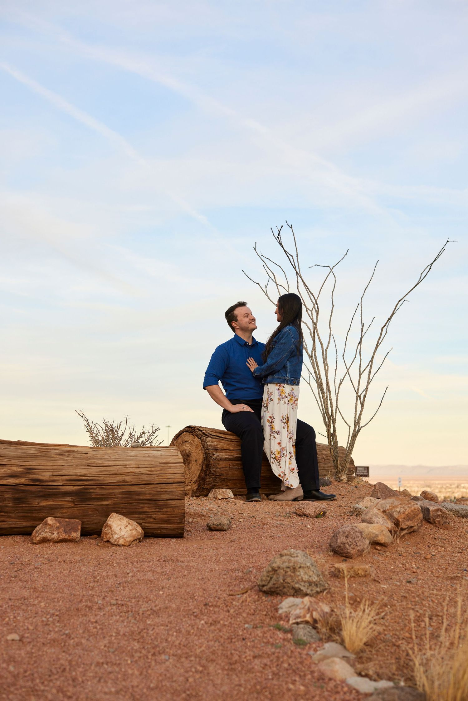 Couple sits together on rocks in desert landscape during golden hour sunset.