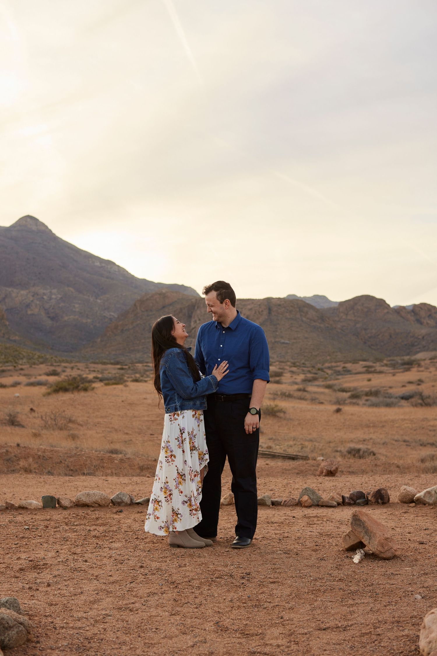 Romantic couple embraces in front of desert mountain landscape at dusk.