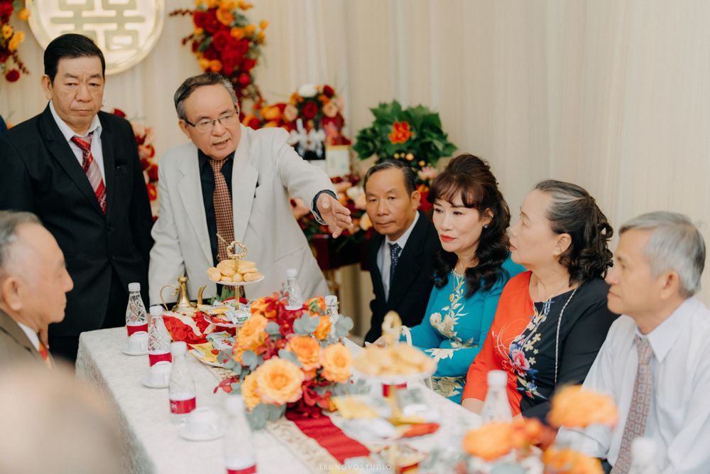 Elegantly dressed guests converse around a decorated table at a traditional Vietnamese wedding reception.