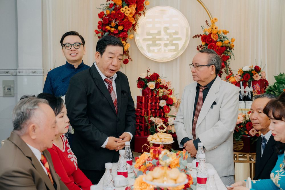 Formally dressed guests gather around festive table at traditional Chinese Vietnamese wedding banquet.