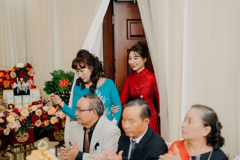 Vietnamese wedding guests in traditional ao dai entering decorated ceremony room with red and gold floral decor.
