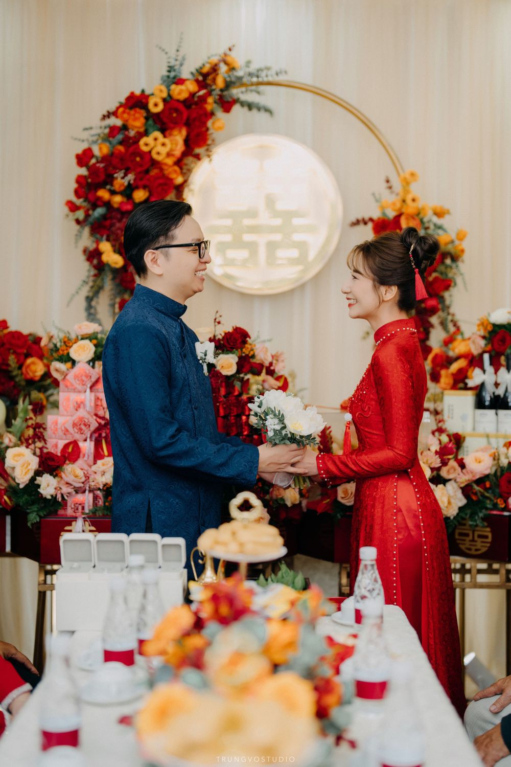 Couple exchanging gifts at Vietnamese traditional wedding ceremony with double happiness symbol backdrop.