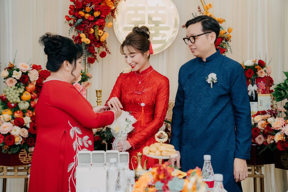 Family members presenting gifts to bride in red ao dai at traditional Vietnamese engagement ceremony.