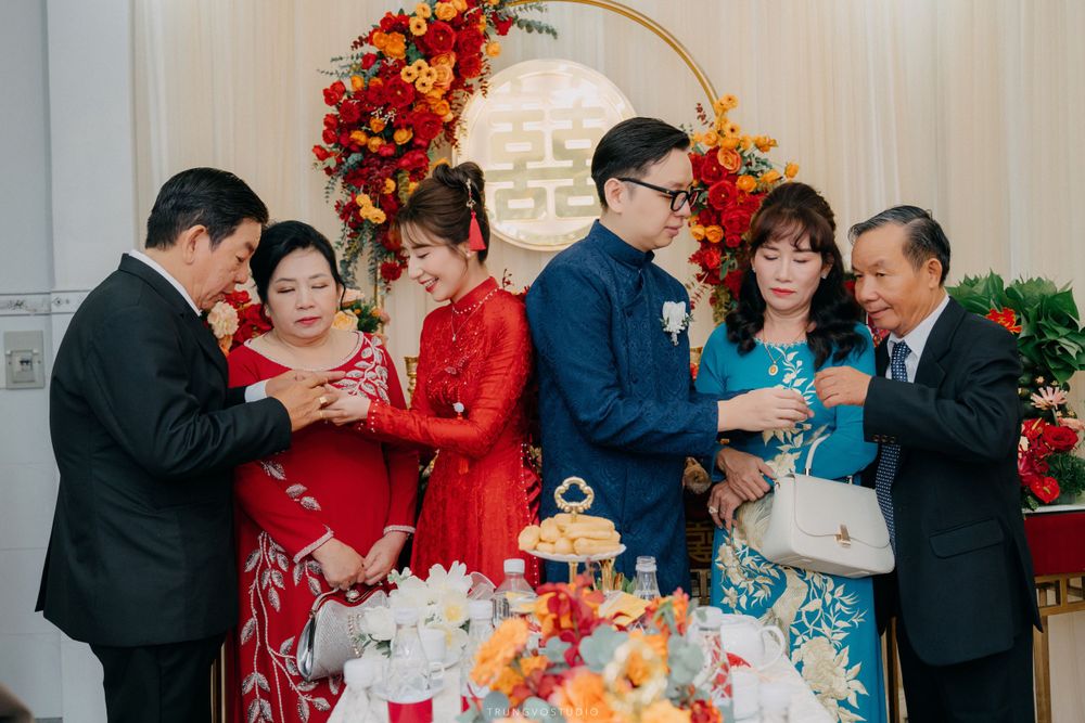 Two families exchanging gifts at Vietnamese traditional engagement ceremony with red floral decorations.