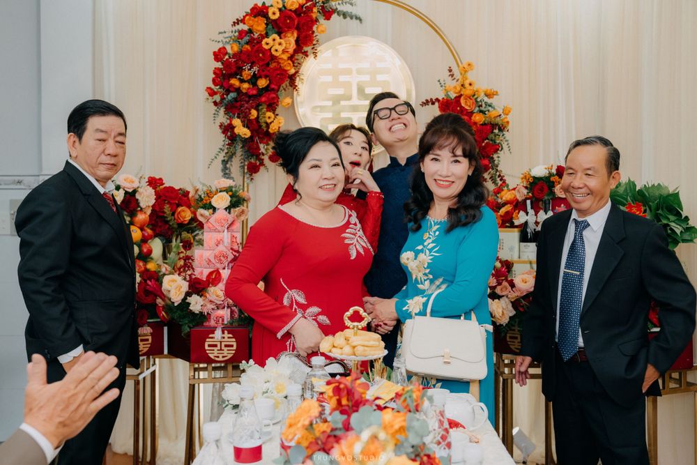 Family members pose together at a vibrant Vietnamese wedding ceremony with red and gold floral decorations.