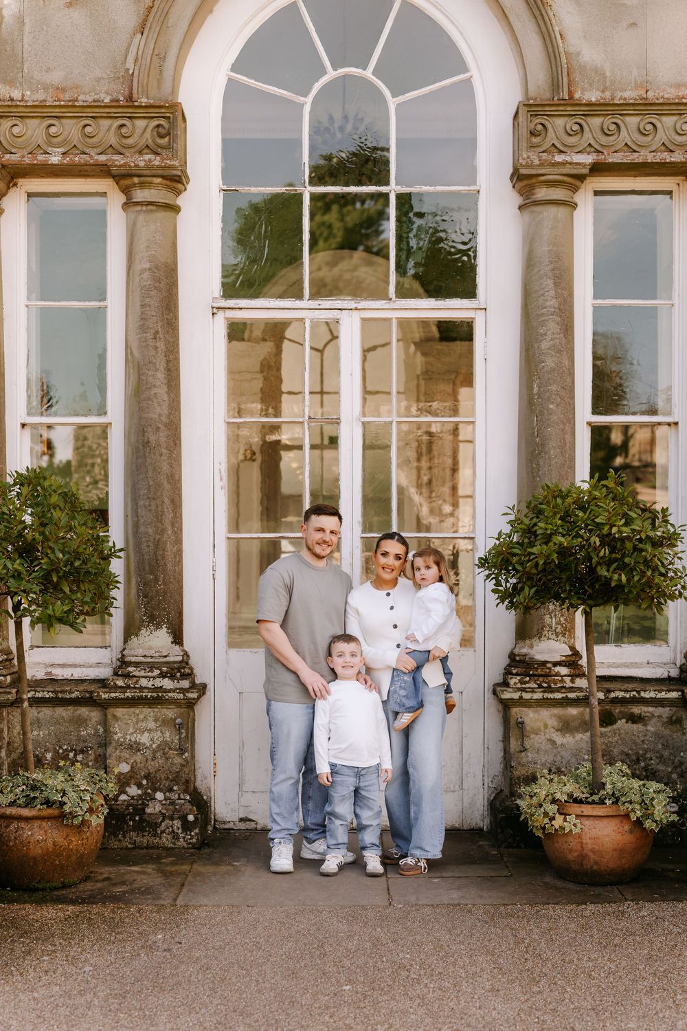 A family stands in front of an elegant arched doorway with ornate columns and potted plants at a historic estate.