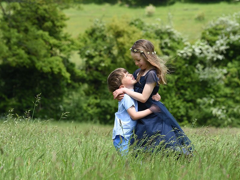 A young boy and girl hug each other in a grassy field, captured in a family photograph by Abigail's studio, Buckinghamshire.